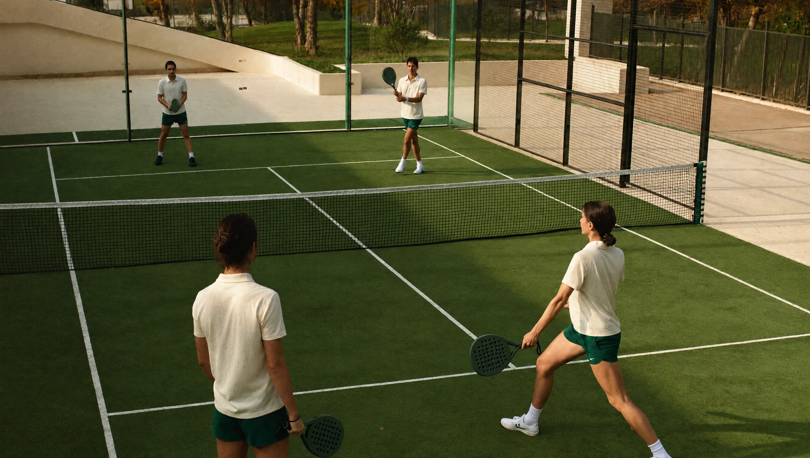 Cuatro jugadores adultos disputan un punto en una cancha verde de pádel.